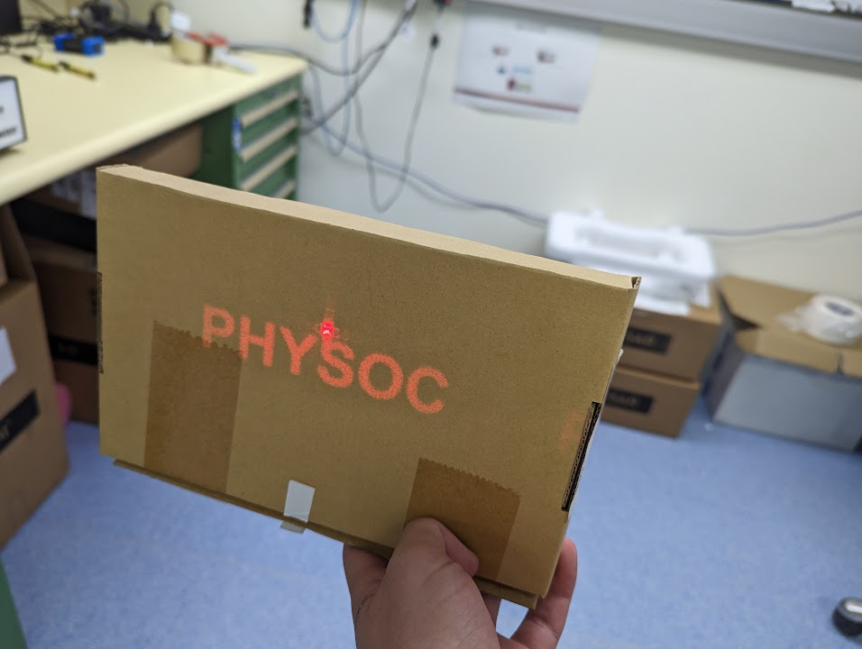 Hologram of the word PHYSOC projected onto a carboard
box